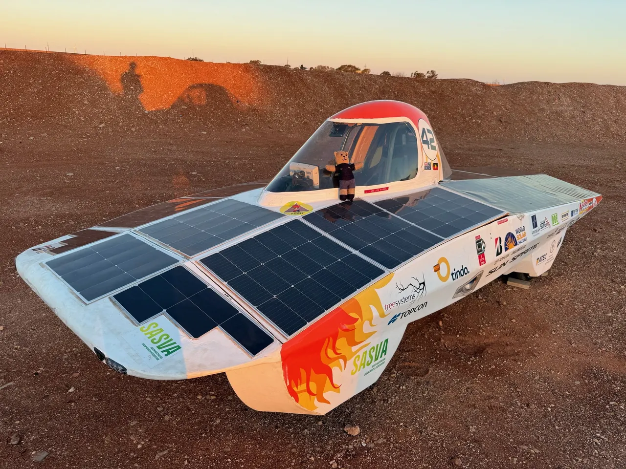 Sun Sprite solar car parked at sunrise in outback Australia, viewed from the front-left with its solar array and number 42 visible.