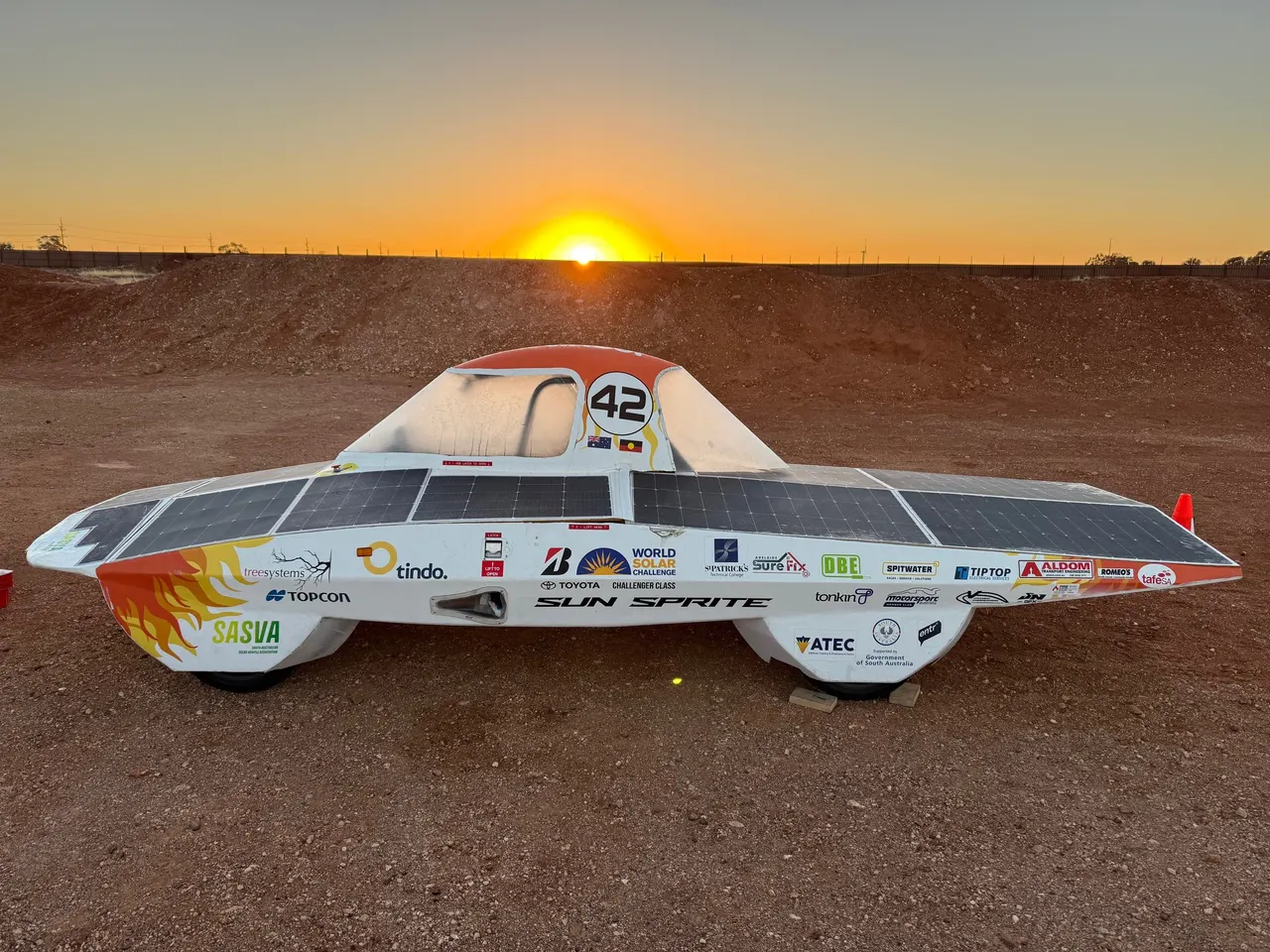 Side profile of SASVA’s Sun Sprite solar car at sunrise, showing the solar array, number 42 and sponsor decals.
